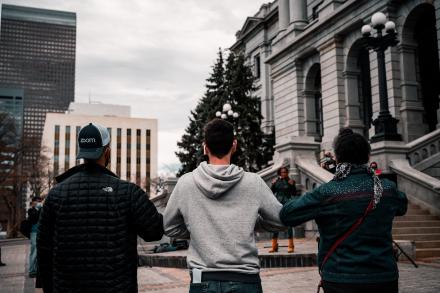 Three people stand arm in arm in front of Colorado Capitol building. Photo by Colin Lloyd on Unsplash.